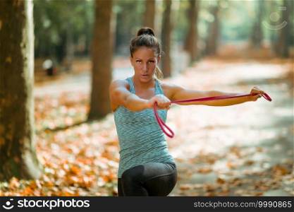 Woman Exercising With Elastic Band Outdoors in The Fall, in Public Park