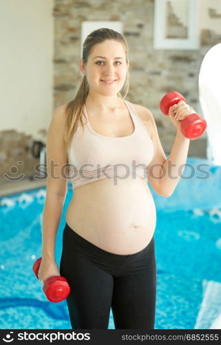 Woman expecting baby doing exercise with dumbbells at gym