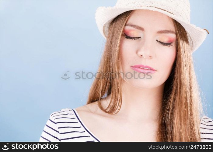 Woman face colorful eye makeup closed eyes straw hat on head smiling having fun closeup. Summer fashion, studio shot on blue. Woman face colorful eyes makeup, summer straw hat smiling
