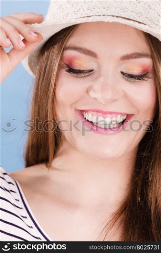 Woman face colorful eye makeup closed eyes straw hat on head smiling having fun closeup. Summer fashion, studio shot on blue