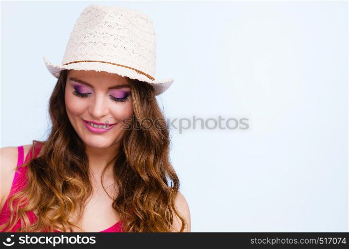 Woman face colorful eyes makeup summer straw hat on head smiling looking down. Summer holidays and happiness, studio shot on blue. Woman in summer straw hat on head smiling