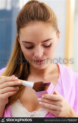 Woman face painting. Girl applying rouge or bronzing powder with brush to her skin in bathroom. Makeup cosmetics and beauty procedures.. Woman applying bronzing powder with brush to her skin