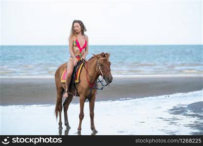 Woman fashion model riding a horse on the beach in summer. Luxury travel vacation.