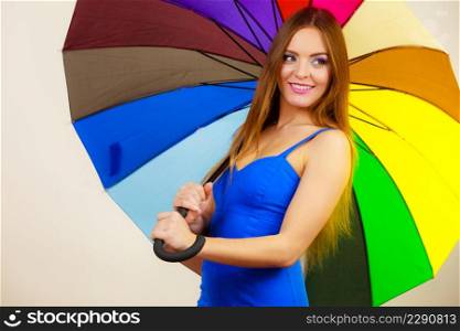 Woman fashion summer attractive girl wearing blue dress standing under colorful rainbow umbrella, on gray. Positive smiling female model. Forecasting and weather season concept. Woman in summer dress holds colorful umbrella