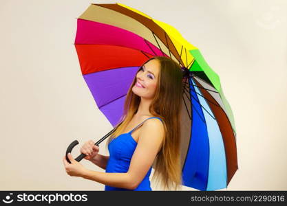 Woman fashion summer attractive girl wearing blue dress standing under colorful rainbow umbrella, on gray. Positive smiling female model. Forecasting and weather season concept. Woman in summer dress holds colorful umbrella