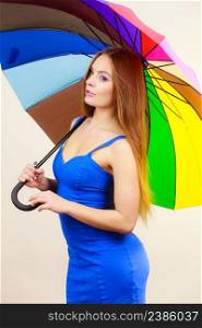 Woman fashion summer attractive girl wearing blue dress standing under colorful rainbow umbrella, on gray. Beautiful female model. Forecasting and weather season concept. Woman in summer dress holds colorful umbrella