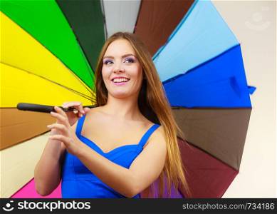 Woman fashion summer attractive girl wearing blue dress standing under colorful rainbow umbrella, on gray. Positive smiling female model. Forecasting and weather season concept. Woman in summer dress holds colorful umbrella