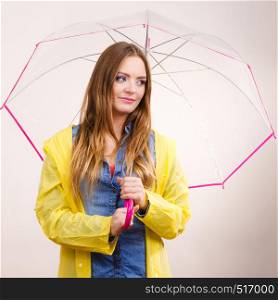 Woman fashionable rainy girl wearing waterproof yellow coat holding transparent umbrella. Meteorology, forecasting and weather season concept. Woman wearing waterproof coat holding umbrella