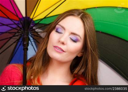 Woman fashionable rainy smiling girl in red clothing standing under colorful umbrella having fun. Meteorology, forecasting and weather season concept. Woman standing under multicolored umbrella