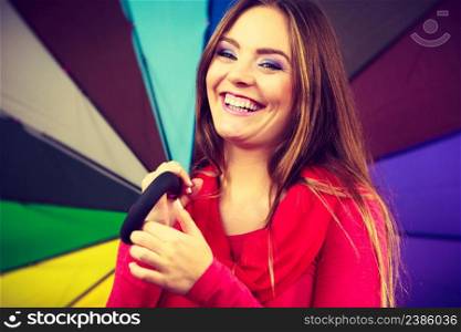 Woman fashionable rainy smiling girl in red clothing standing under colorful umbrella having fun. Meteorology, forecasting and weather season concept. Woman standing under multicolored umbrella