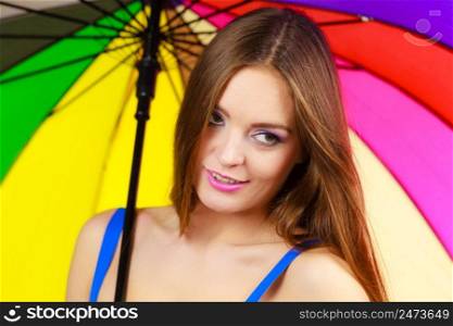 Woman fashionable summer girl standing under colorful rainbow umbrella, close up. Attractive female long hair model. Forecasting and weather season concept. Woman standing under colorful rainbow umbrella