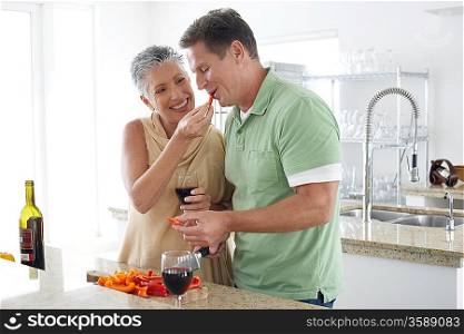 Woman feeding pepper to husband in kitchen