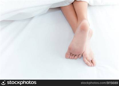 Woman feet on the bed under white blanket. Sleeping and relax concept. Vacation and Holiday theme