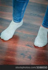 Woman feet standing on wooden floor wearing blue jeans and light socks.. Unrecognizable woman wearing socks