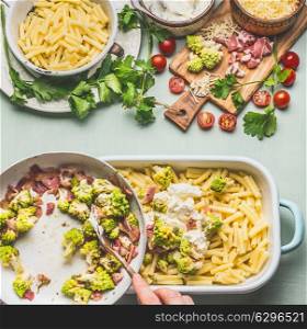 Woman female hands cooking pasta casserole with roasted romanesco cabbage and ham in creamy sauce on kitchen table background with ingredients, top view . Italian cuisine