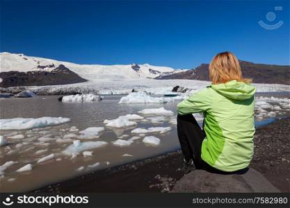 Woman female hiker wearing a green jacket sitting on a rock looking out on a melting glacier and icebergs in Iceland
