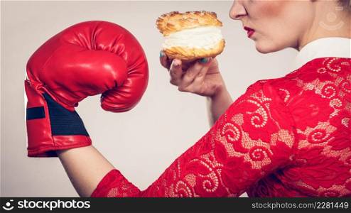 Woman fighting with her bad habits, being on diet. Female wearing boxing glove holding sweet dessert, cream cupcake.. Woman boxing cream cupcake