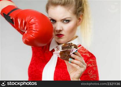 Woman fighting with her bad habits, being on diet. Female wearing boxing glove holding sweet dessert, chocolate cupcake.. Woman boxing chocolate cupcake