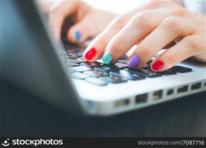 Woman fingers with colorful polished nails are typing on a laptop keyboard