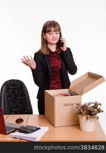 Woman fired from her job at the office collects personal belongings in a box and talking on the phone. Girl in office collects personal belongings and calling on phone