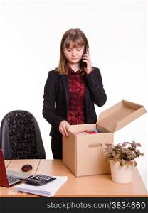 Woman fired or hired in the office and collect or parses personal belongings out of the box and is calling on the phone. Girl in office examines personal things and calling on phone