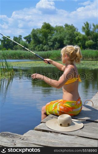 Woman fishing in the river on an old, wooden jetty