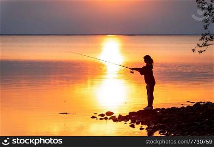 Woman fishing on Fishing rod spinning in Finland at sunset.