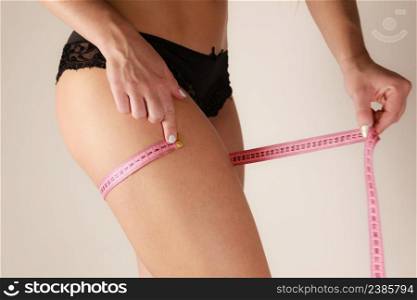 Woman fit girl in black lingerie measuring her thigh with measure tape closeup. Part of female body. . Woman measuring her thigh closeup