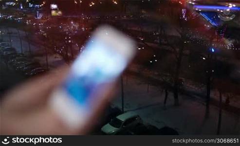 Woman flipping through the pictures in her smartphone near the window with view of city traffic. Zooming in on some pictures. Focus on the city, than on the phone.