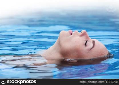 Woman floating in pool. Close up view of an attractive young woman floating in swimming pool