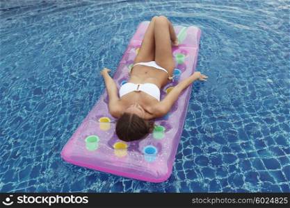 Woman floating in pool. Close up view of an attractive young woman floating in swimming pool on waterbed