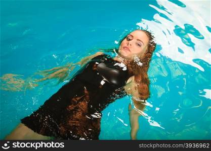 Woman floating relaxing in swimming pool water.. Woman relaxing at swimming pool. Young girl wearing black dress floating. Water aerobics fitness.