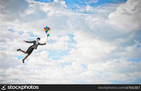 Woman flying in sky. Young businesswoman in suit and bowler hat flying on windmill