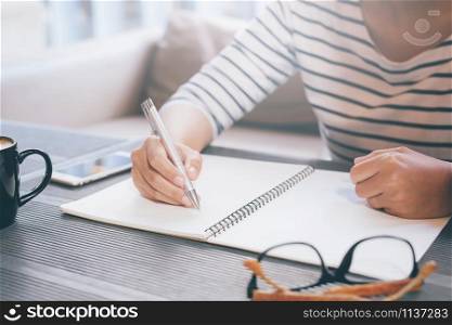 Woman freelancer working hand writing journal on small notebook notepad in coffee shop using with copy space area.