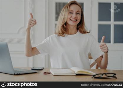 Woman gestures thumb sitting at computer. Happy mid adult businesswoman is working from home. Attractive blond european lady is working on nice laptop. Concept of good device and remote work.. Woman gestures thumb working on nice laptop. Concept of good device and remote work.