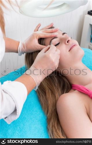 Woman getting tweezing eyebrow by beautician