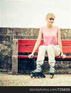 Woman girl with roller skates blades sitting on bench outdoor.. Woman with roller skates outdoor.
