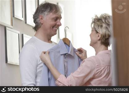 Woman giving shirt to smiling mature man while standing at home
