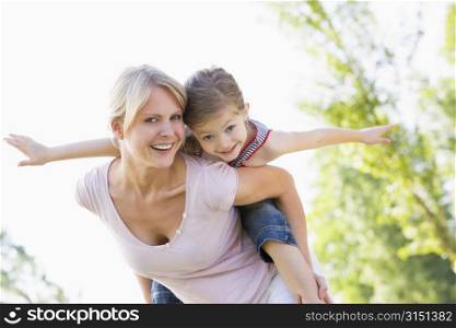 Woman giving young girl piggyback ride outdoors smiling
