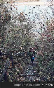 Woman going upstairs on trekking path during trip on autumn. Active middle aged woman with backpack actively spending autumnal season. Woman going upstairs on trekking path during trip on autumn