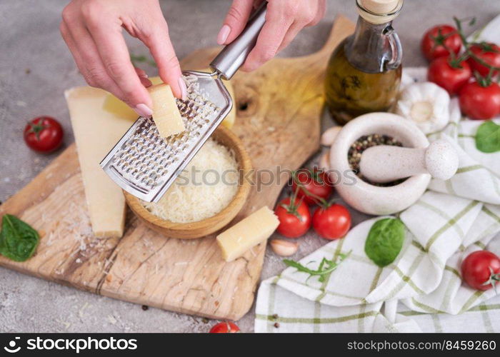 Woman grates Parmesan cheese on a wooden cutting board at domestic kitchen.. Woman grates Parmesan cheese on a wooden cutting board at domestic kitchen