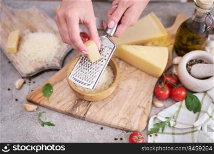 Woman grates Parmesan cheese on a wooden cutting board at domestic kitchen.. Woman grates Parmesan cheese on a wooden cutting board at domestic kitchen