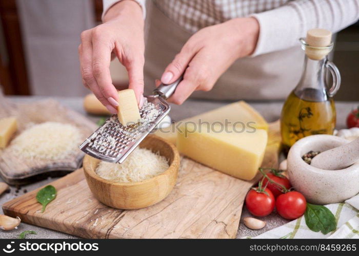 Woman grates Parmesan cheese on a wooden cutting board at domestic kitchen.. Woman grates Parmesan cheese on a wooden cutting board at domestic kitchen