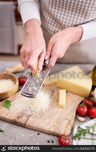 Woman grates Parmesan cheese on a wooden cutting board at domestic kitchen.. Woman grates Parmesan cheese on a wooden cutting board at domestic kitchen