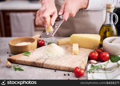 Woman grates Parmesan cheese on a wooden cutting board at domestic kitchen.. Woman grates Parmesan cheese on a wooden cutting board at domestic kitchen