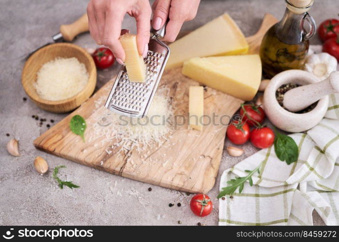 Woman grates Parmesan cheese on a wooden cutting board at domestic kitchen.. Woman grates Parmesan cheese on a wooden cutting board at domestic kitchen