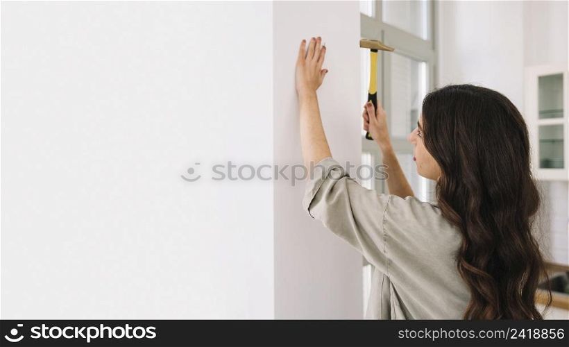 woman hammering nail wall