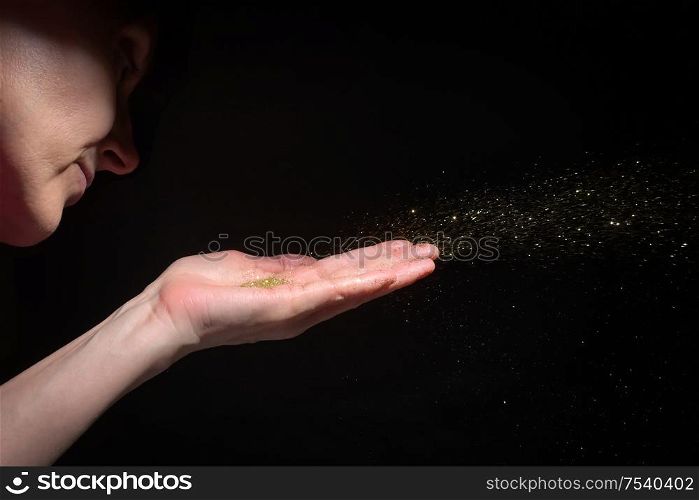 Woman Hand Blowing Glitter Sparkles on Black Background