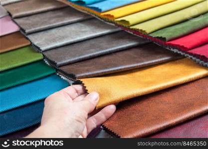 Woman hand chooses samples of colored fabric on table close up. Woman hand chooses samples of colored tissue
