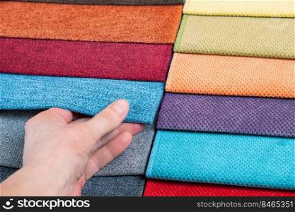 Woman hand chooses samples of colored fabric on table close up. Woman hand chooses samples of colored tissue
